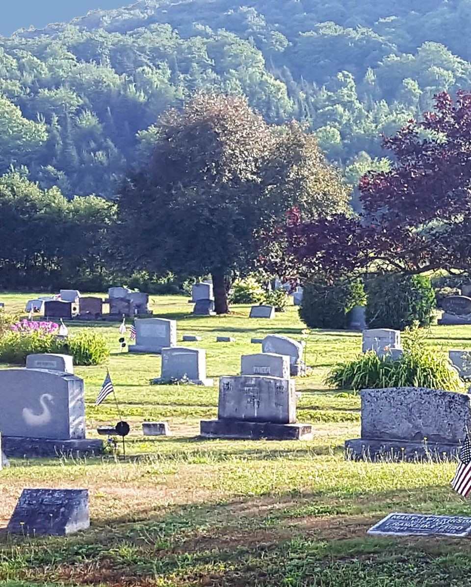 Hillside cemetery with headstones, trees, and small American flags