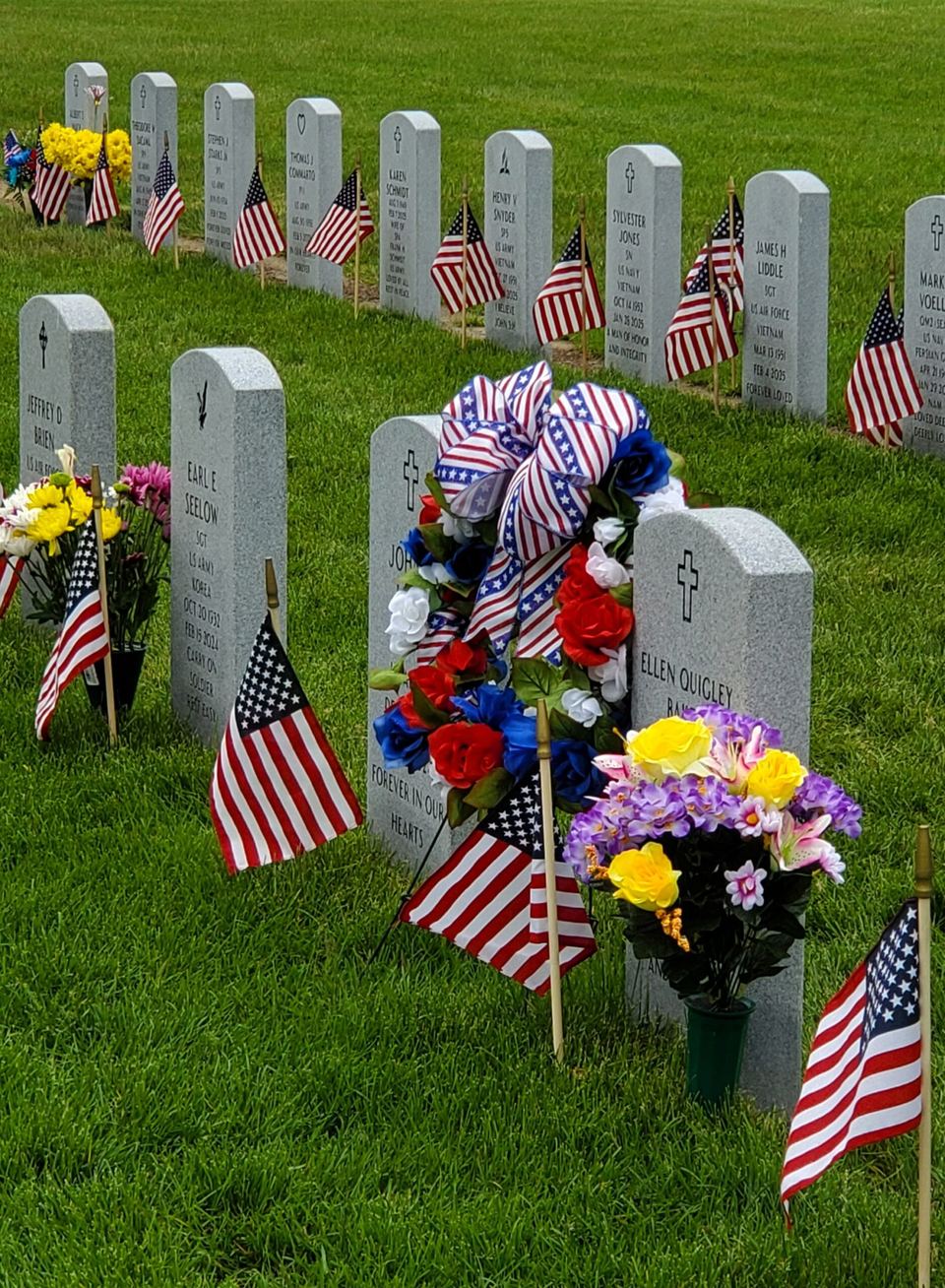 Veterans cemetery headstones with American flags, flowers, and a patriotic wreath
